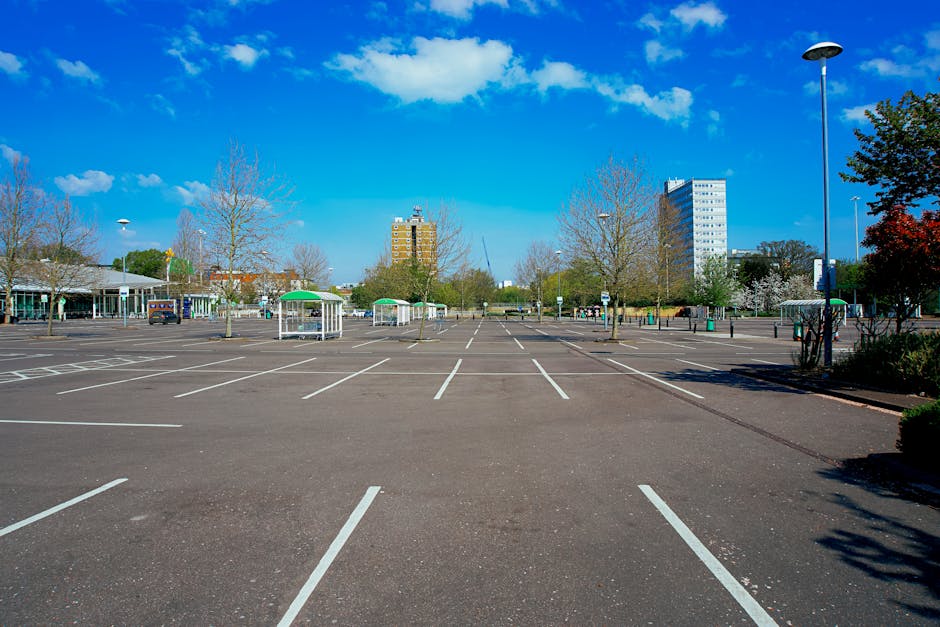 A row of parked cars along a residential street with pavement, some new or recently cleaned, under an overcast sky. The vehicles include various sizes and colours, parked adjacent to a multi-storey brick building with commercial establishments on the ground floor. In the background, there are leafless and lush green trees, indicating early spring or late autumn. The street is compliant with parking regulations, with a clear no-entry sign visible at the end. This parking arrangement is suitable for house removals and furniture transport, supporting logistic planning for a home relocation. Occasionally, Man with Van Park Royal might use this area for loading or unloading household furniture and boxes during local removals, although no activity is visible in this particular image.